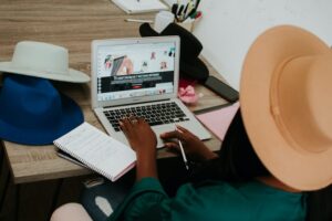 photo of a stylish blogger writing on a computer. The desk, notebooks and some hats can be seen. The blog post is about the topic which is better vlogging or blogging