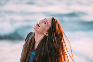 Happy woman, laughing next to the see. Th blog post relates how to change your life