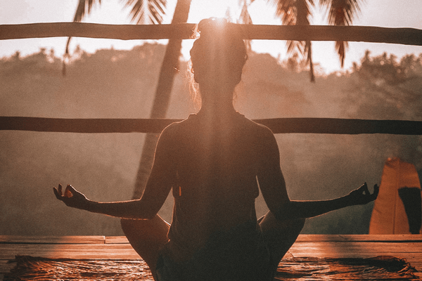 A woman meditates, sun is shining, palm trees. Learn how to improve yourself everyday.