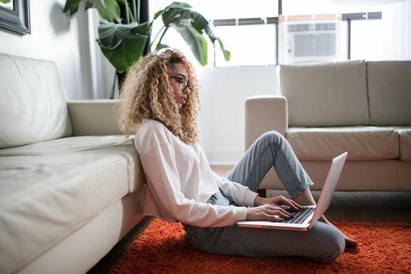 Woman sitting on the ground at home and working on her laptop. Learn about productive things to do on computer when bored