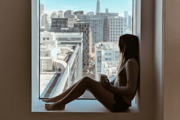 A girl sitting next to the window, looking at NY and thinking about different ways to stop overthinking