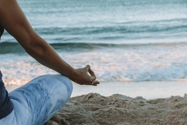 woman meditating on the beach and thinking about how to be mindful in your daily life